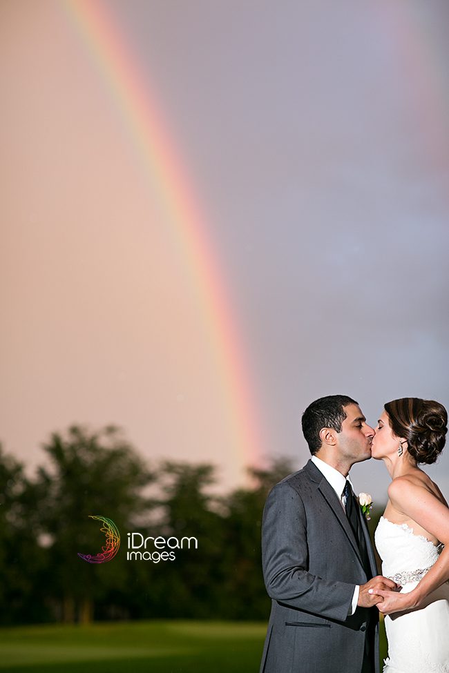 Bride and groom kissing under a rainbow